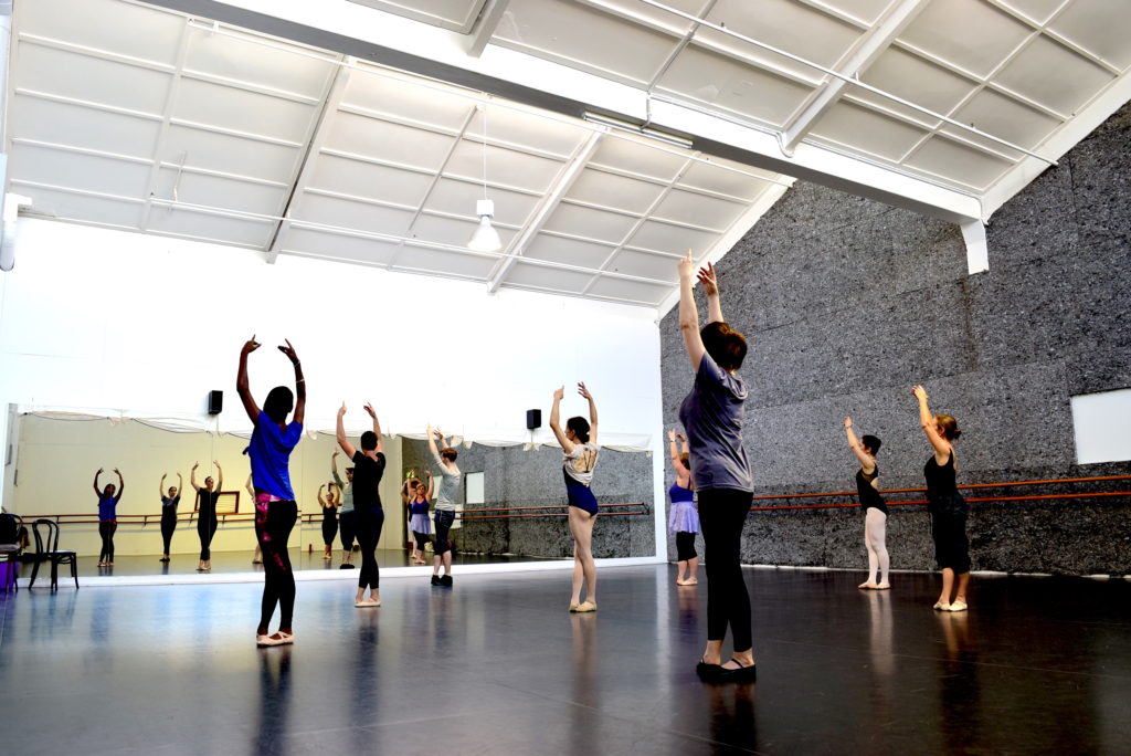 Adult ballet dancers in a dance studio in North Melbourne with arms up in fifth position looking into the mirror