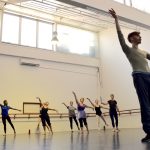 Adult ballet dancers dancing in a group behind male ballet teacher