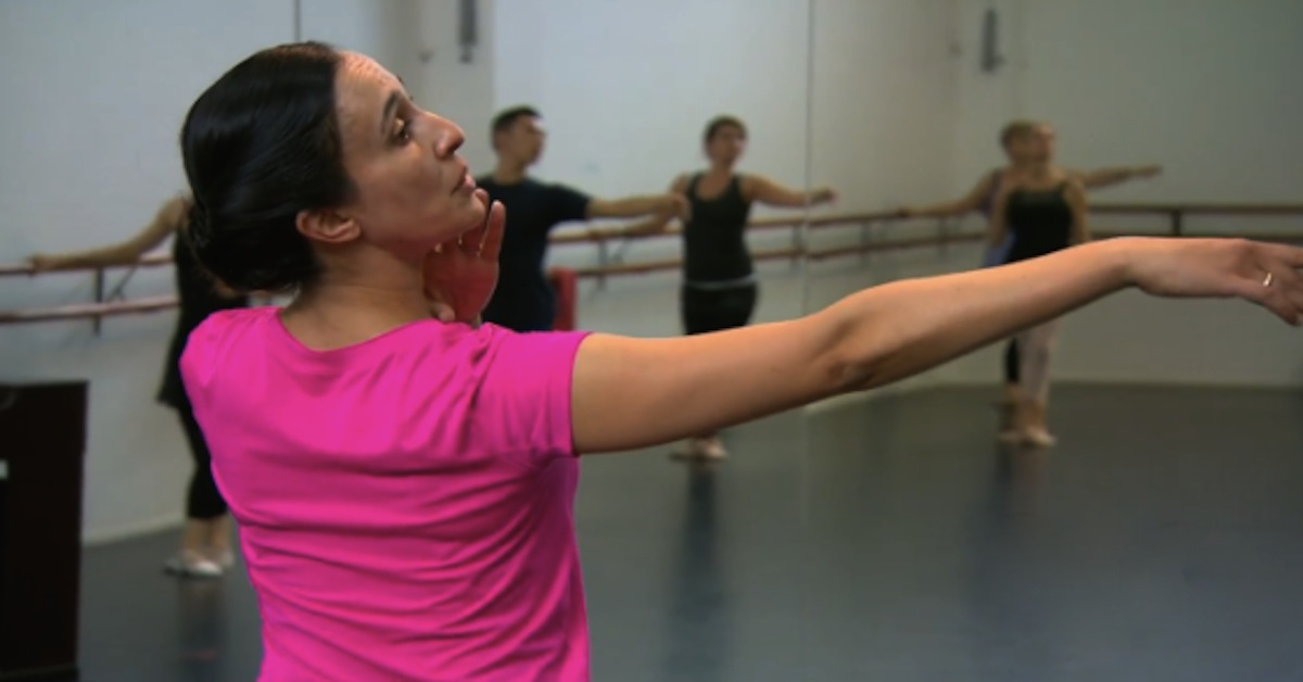 Ballet teacher in pink shirt looking along extended arm