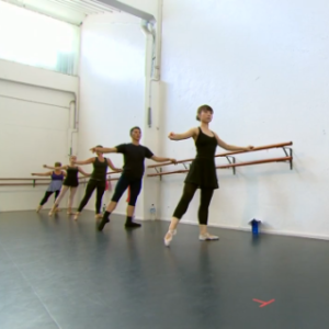 adult ballet dancers with one leg out to the side holding onto a wooden ballet barre